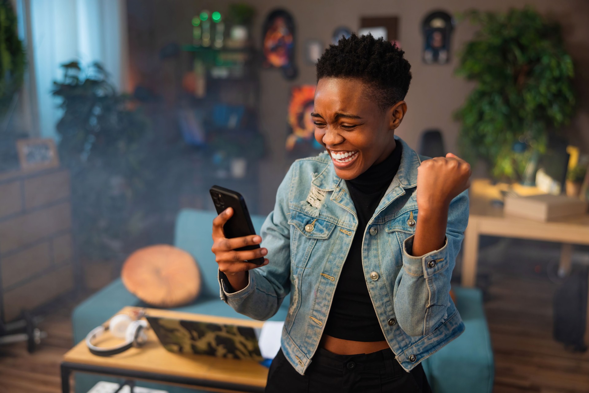 Happy african american teen girl lady woman with short hair using cell phone holding in hands smiling celebrating raising fists