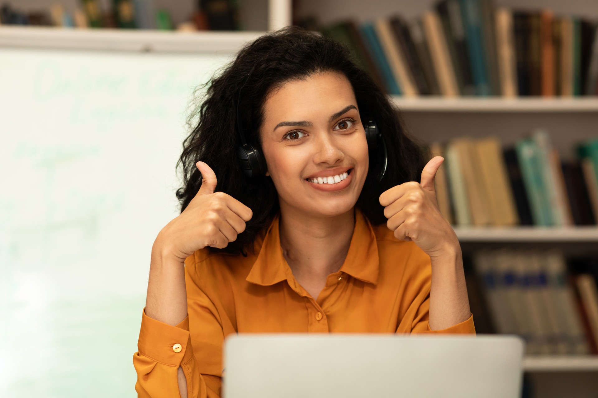 Online teacher. Happy mixed race female tutor in headphones showing thumbs up, looking and smiling at camera